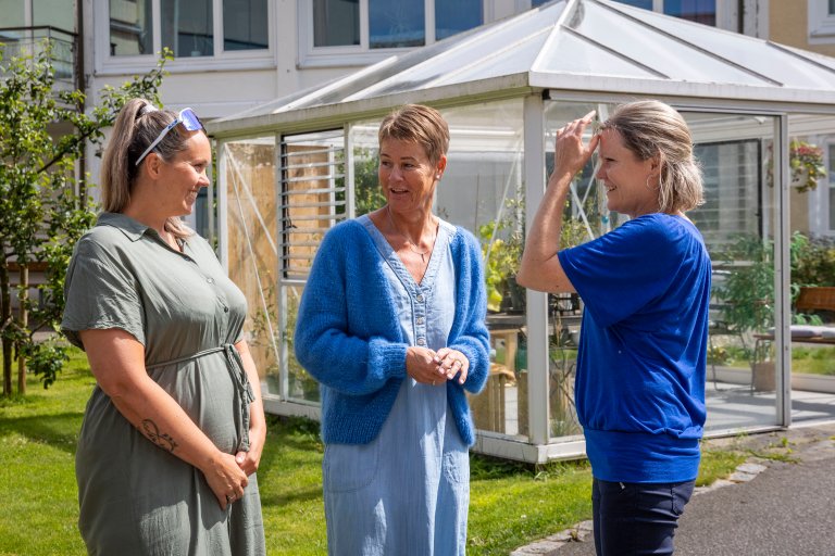 Tre kvinner står og snakker sammen utendørs. De ser engasjerte og glade ut.