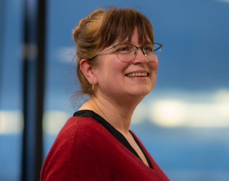 Foto av en kvinne med brunt hår og briller. Hun smiler.